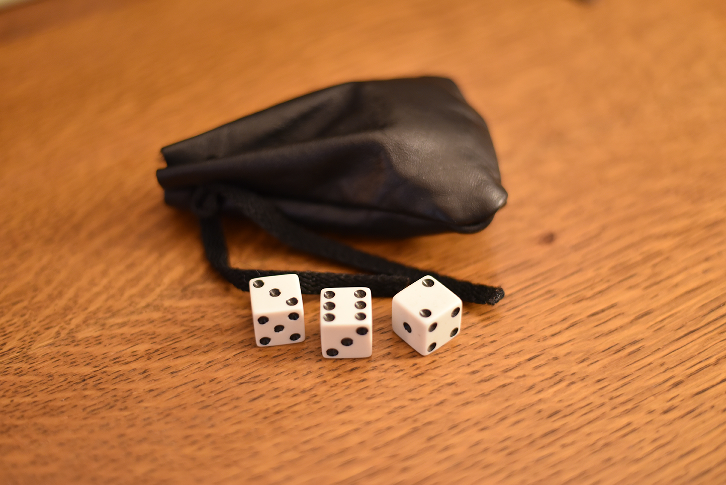 Three six sided dice next to a black leather dice bag.